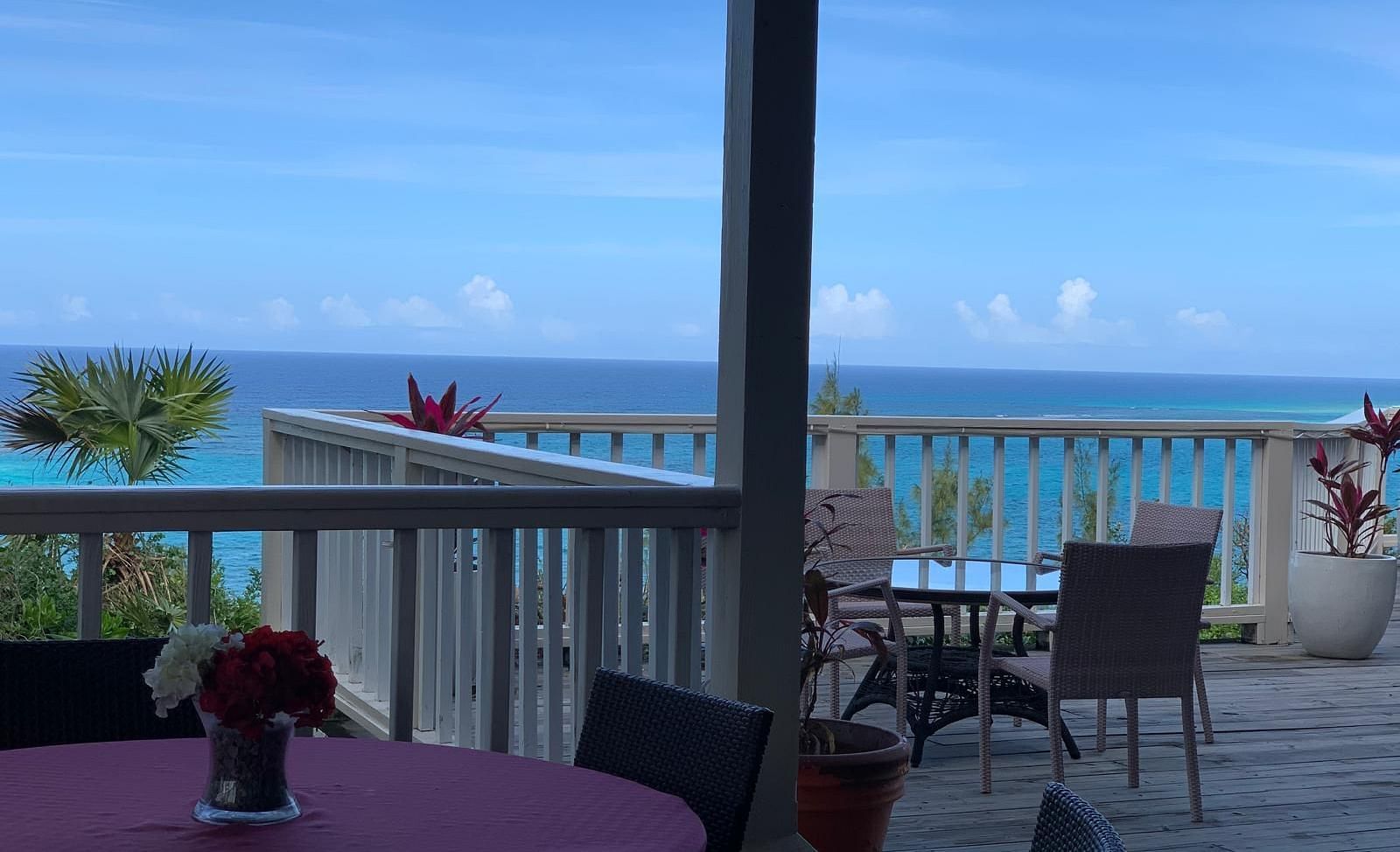Patio with tables and chairs, flower centerpieces on the tables, and ocean visible beyond railing | A Stone's Throw Away