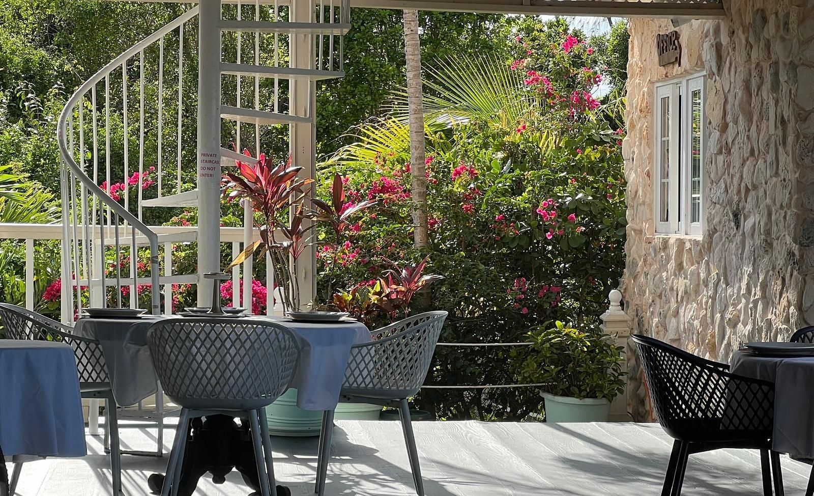 Outdoor dining area with black chairs and spiral staircase surrounded by lush plants | A Stone's Throw Away