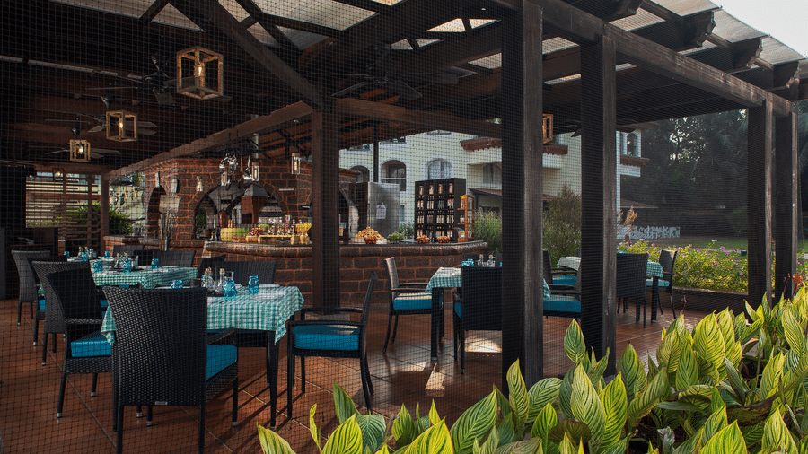 Wooden pergola dining area framed by lush green plants at Kenilworth Resort & Spa, Goa.