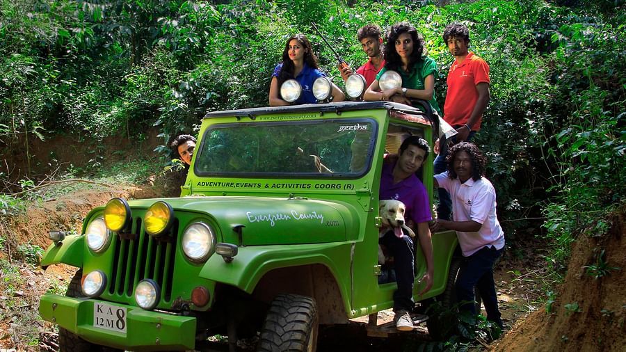 A group of people posing on and around a green jeep on a muddy track in a lush forest - Evergreen County