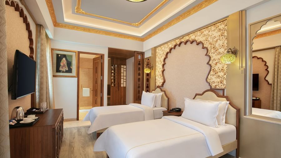 A room with twin beds, ornate golden accents, and a decorative wall panel – Kaldan Samudra, a luxurious beach resort in ECR