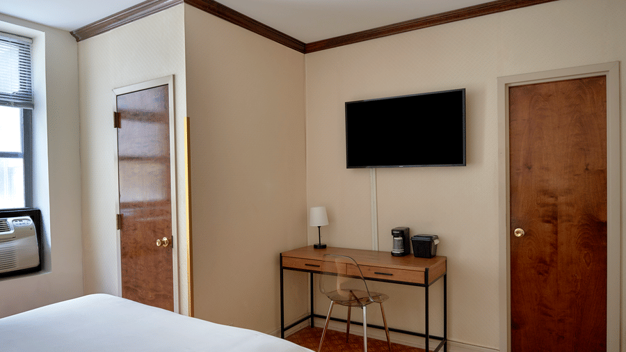 Guest room at Night Hotel Broadway with a mounted TV, desk, chair, and bed in view.