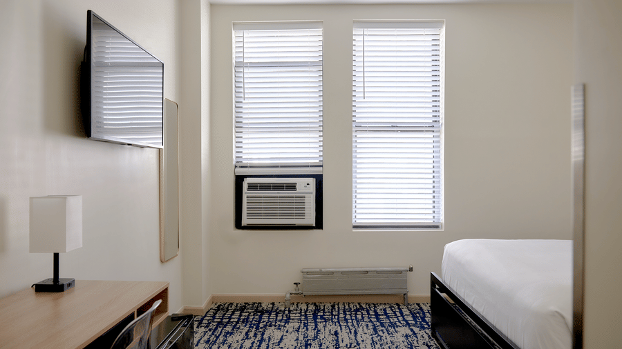 Bright room at Night Hotel Broadway with single bed, TV, air conditioner, and window.