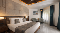 A view of the Junior Suite with a king bed, side tables, side lamps, ceiling fan and chairs in the corner at Kenilworth Resort & Spa, Goa.