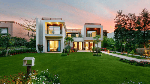 Facade view of the Woodpecker Villa at Karma Lakelands with a green lawn and garden in front.