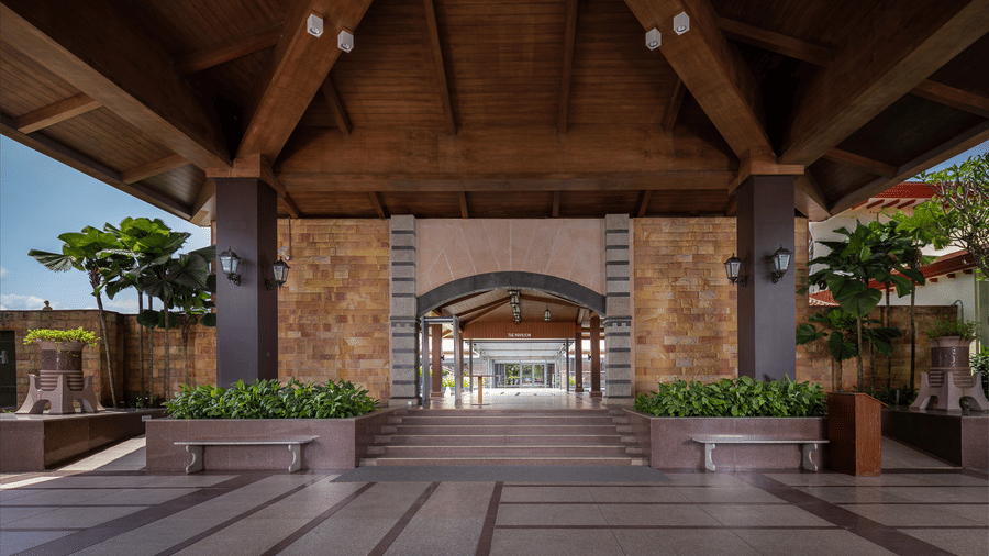 A view of the entrance view Kenilworth Resort and Spa, Goa, featuring stairs leading to the interiors of the resort, and potted plants on the pillars supporting the roof. The resort is know to be the best place for a workation in Goa.