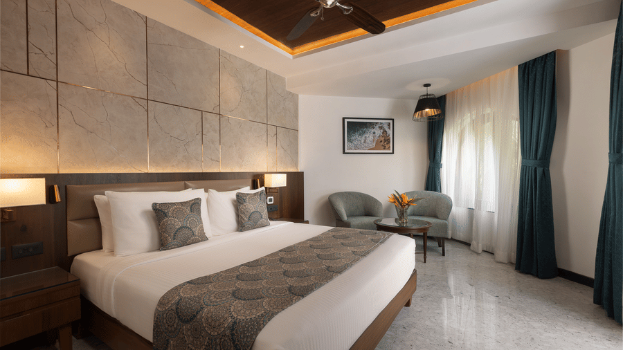 A view of the Junior Suite with a king bed, side tables, side lamps, ceiling fan and chairs in the corner at Kenilworth Resort & Spa, Goa.