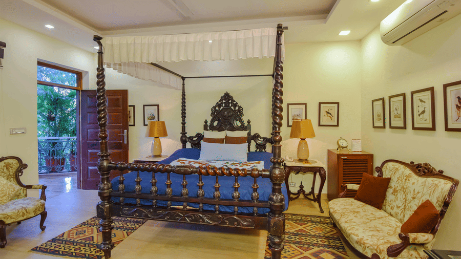 A room at the Shaheen Bagh resort featuring a plush wooden bed, wooden chairs, side tables, and a door leading to the balcony.