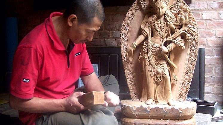 An overview of a man sculpting an idol from wood with accurate hits of the hammer.