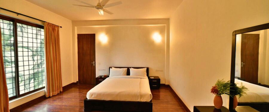 A spacious bedroom in Aqua Bungalow with warm lighting and wooden flooring at Vedic Village Spa Resort.