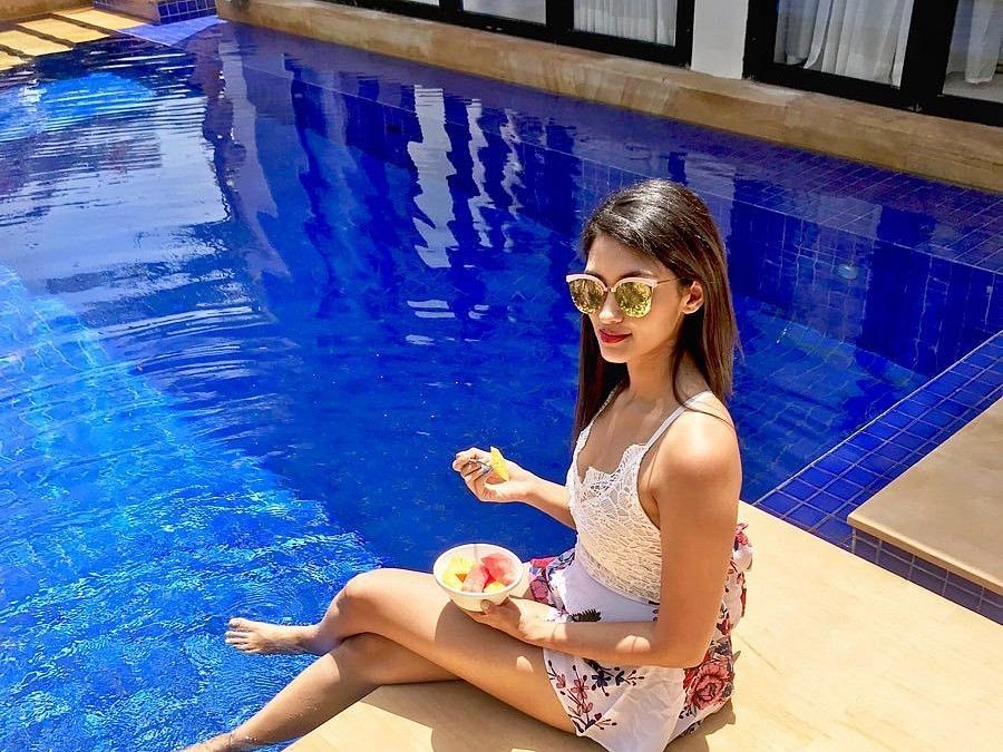 Lady with sunglasses lounging by the pool enjoying a fruit bowl