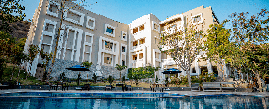 Facade of Essentia Luxury Resort and Spa, Udaipur with the pool in front of it.