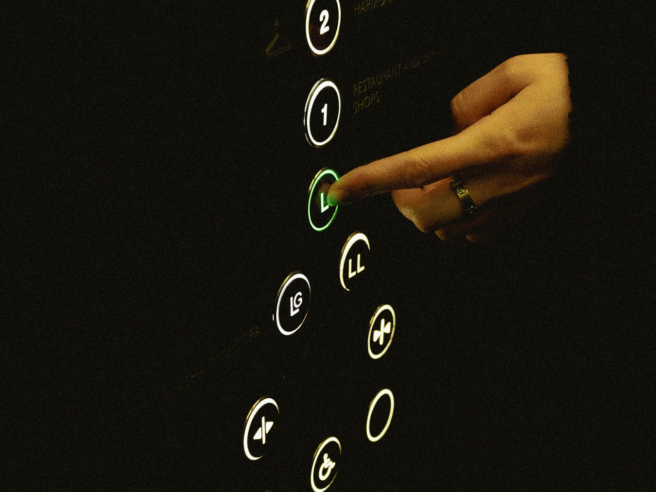 Hand pressing a lit elevator button on a dark control panel.