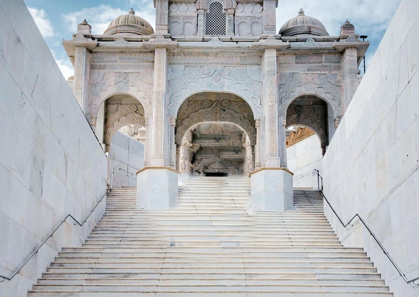 Entrance to a Jain temple made of marble with a large staircase during the day.