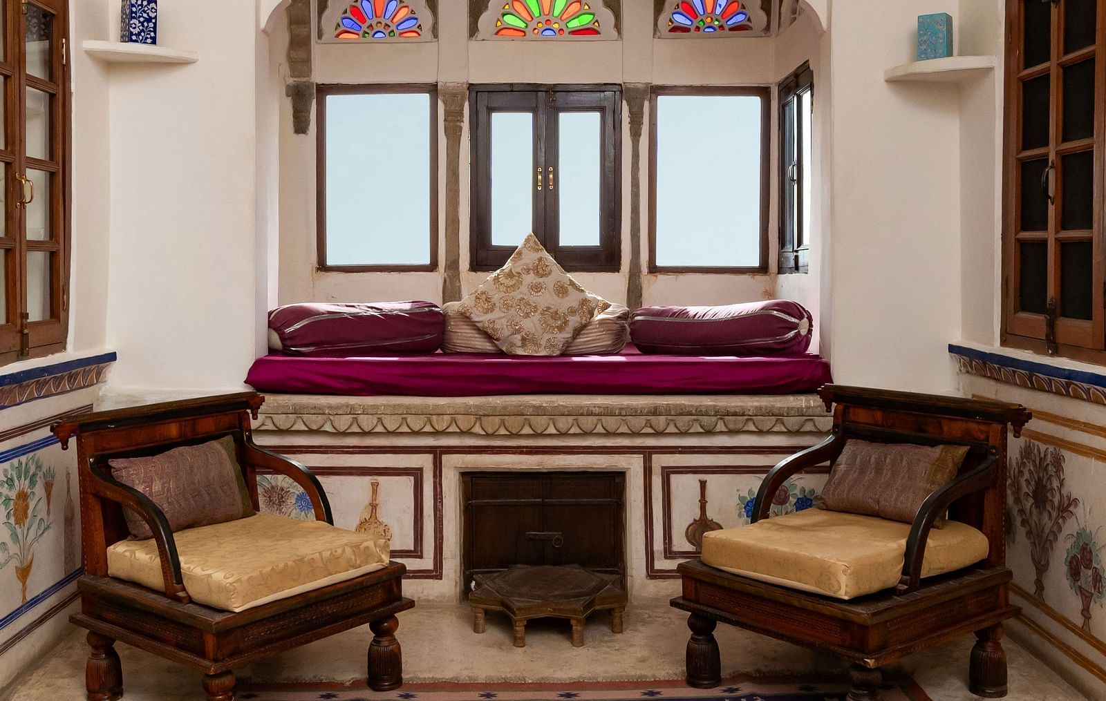 A cozy seating area at Fort Barli, Ajmer, features a cushioned alcove, chairs, and a patterned rug.