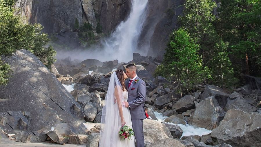 A couple posing for a wedding photoshoot in front of a waterfall in Yosemite - Narrow Gauge Inn - A Serenite Hotel Near Fish Camp.