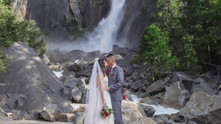 A couple posing for a wedding photoshoot in front of a waterfall in Yosemite - Narrow Gauge Inn - A Serenite Hotel Near Fish Camp.