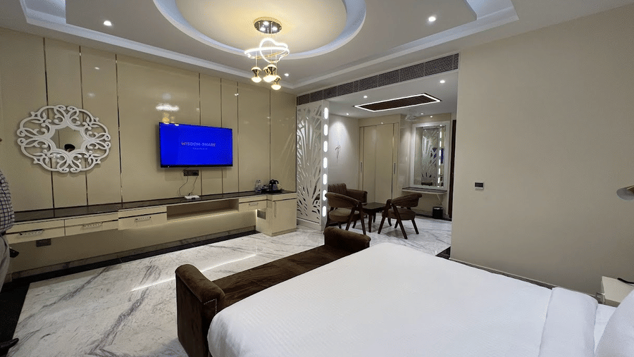 Bedroom of Lime Tree Hotels & Service Apartment Private Limited featuring pendant lighting, a wall mounted television, and white bedding.