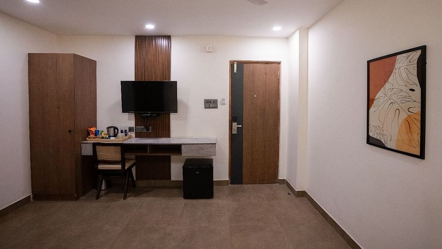 A room featuring a workspace with a desk, TV, wardrobe, and cozy lighting, ideal for relaxation and productivity at Hotel Kyzen Smartstays – Smart, Reliable, Kyzen