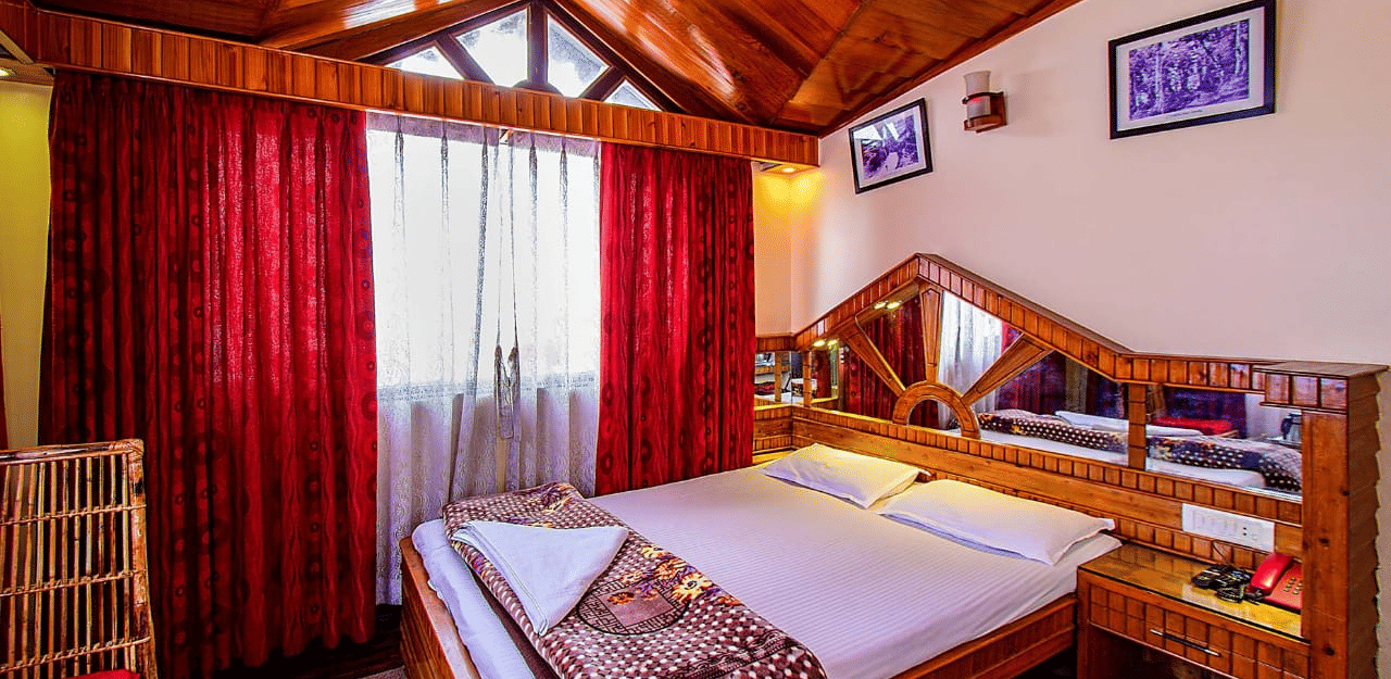 Room featuring a wooden vaulted ceiling, double bed, red curtains, and a wooden dressing table with a large mirror at Hotel Dolphin Darjeeling.
