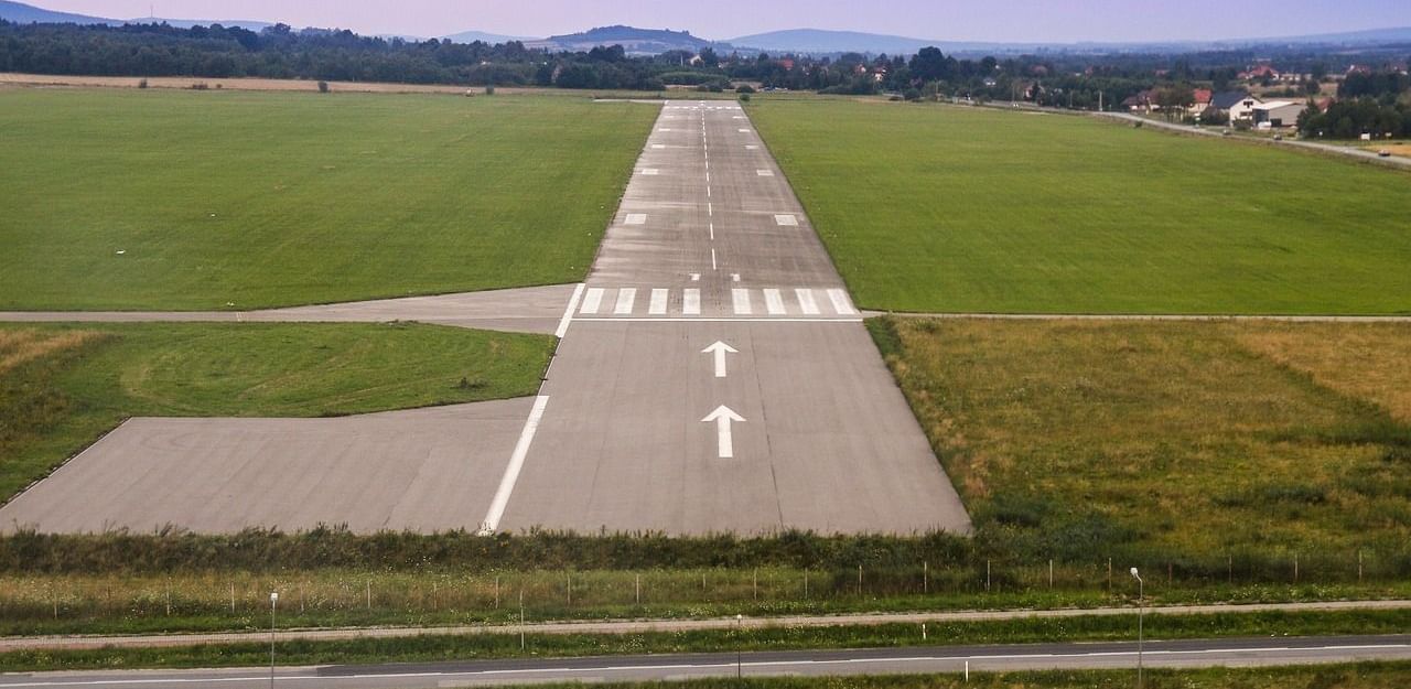 A small runway in the middle of a grassy field, with white markings and a distant view of rolling hills and sky.