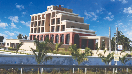 Multi-storey modern hotel building exterior of Lords Swastik Studio, Kodinar, surrounded by plants under a bright sky.