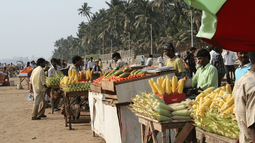 A beachside market with vendors selling fruits and coconuts under palm trees.