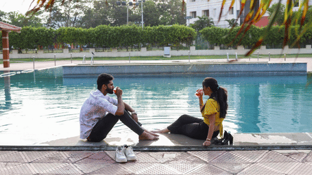 A couple sitting at the edge of a large swimming pool, enjoying drinks in a tranquil outdoor setting - Jenneys Residency, Coimbatore