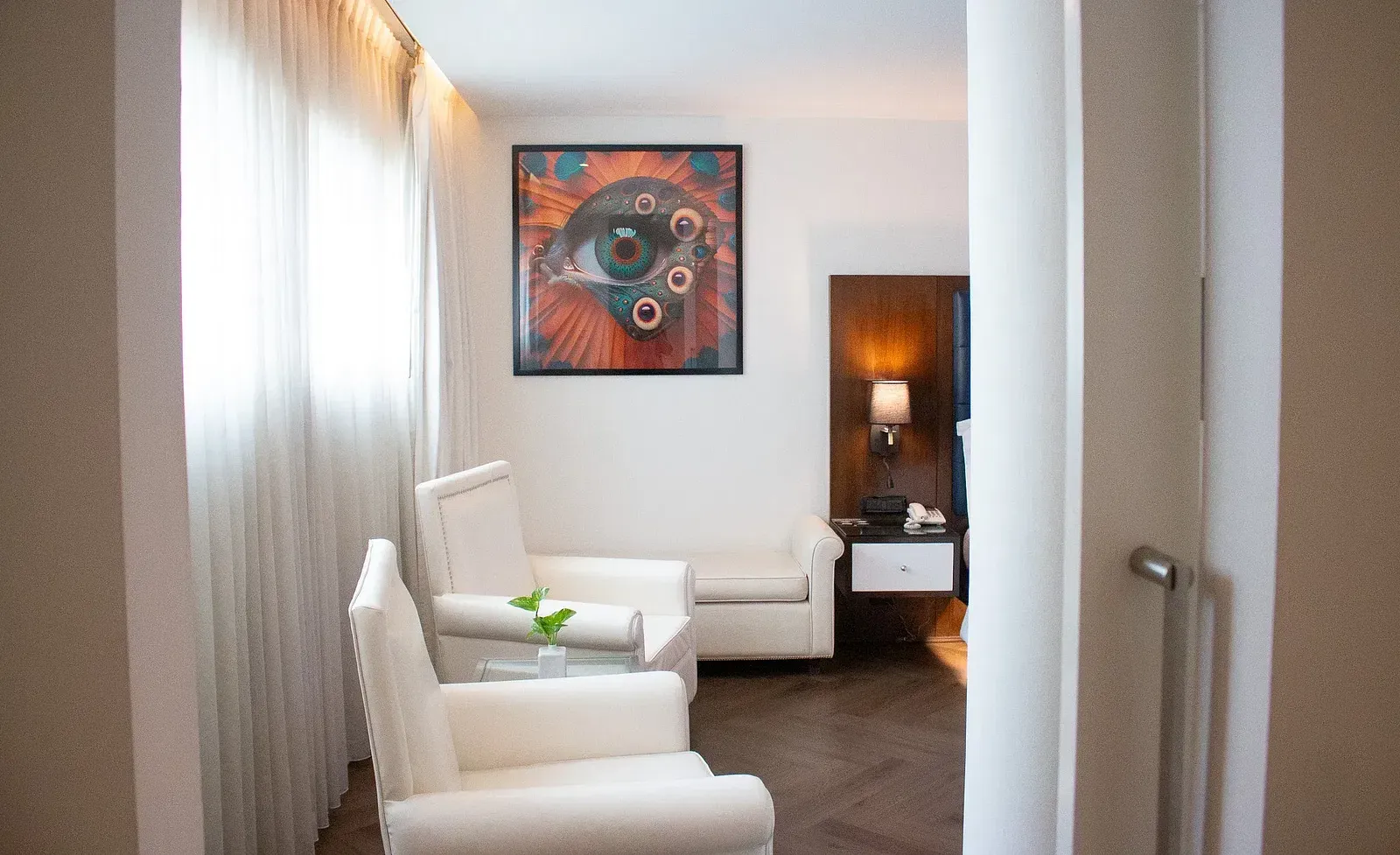 Stylish hotel seating nook with cream armchairs, colourful abstract artwork, walnut side table, and floor-to-ceiling windows with natural light at Night Hotel Bangkok.