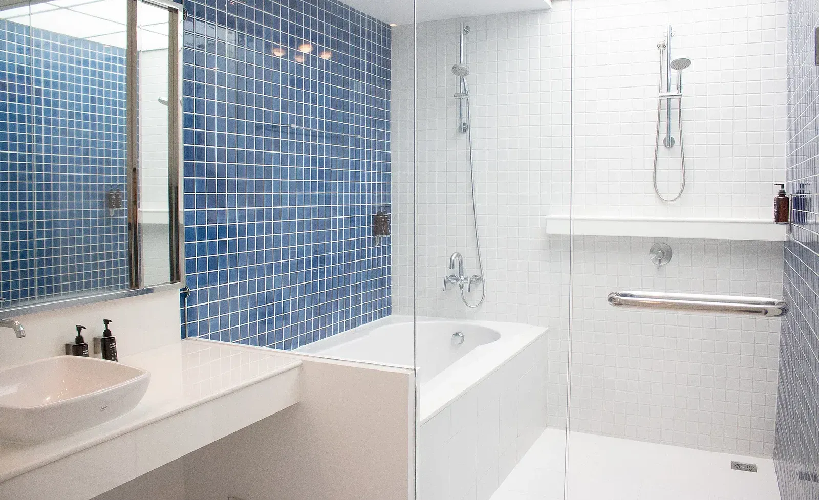 Spacious hotel bathroom featuring blue mosaic tiles, white subway tiles, modern bathtub, rainfall shower, and clean contemporary design aesthetic at Night Hotel Bangkok.