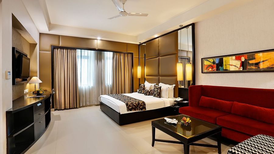 A spacious junior suite with a sleek design, featuring a large bed, red sofa at The Manor, Bareilly