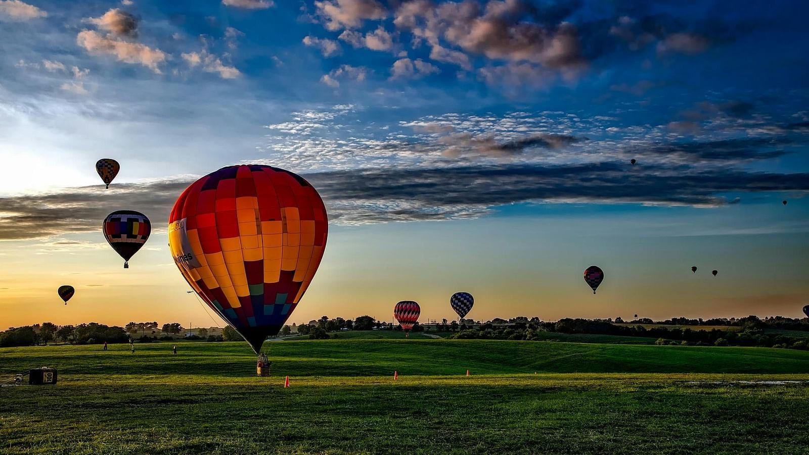 Shot of a cluster of colourful hot air balloons soar through the sky at sunset.