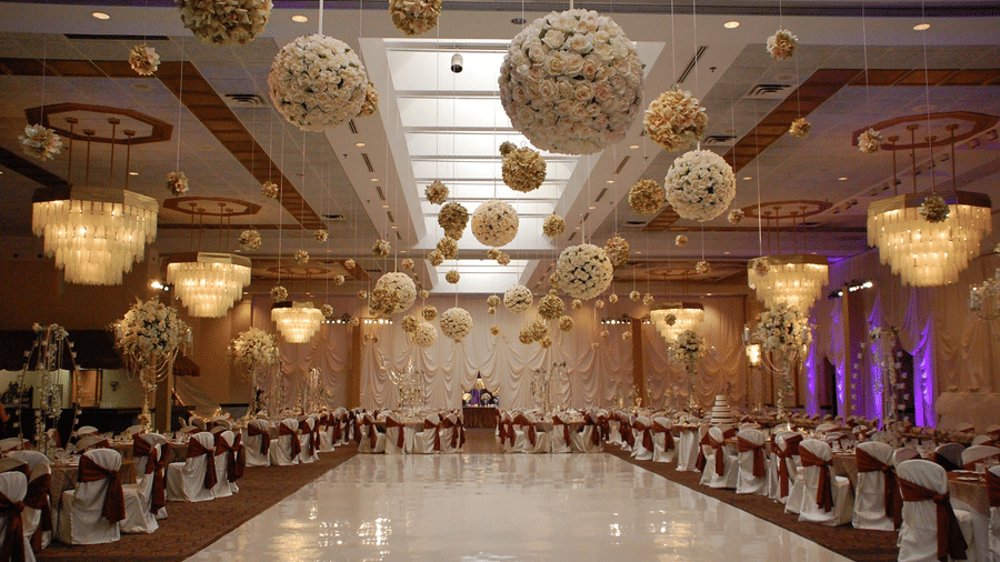 Wedding venue with ornate crystal decorations featuring crystal chandeliers, chairs and tables covered with white satin cloth, and floral decorations hanging from the ceiling.