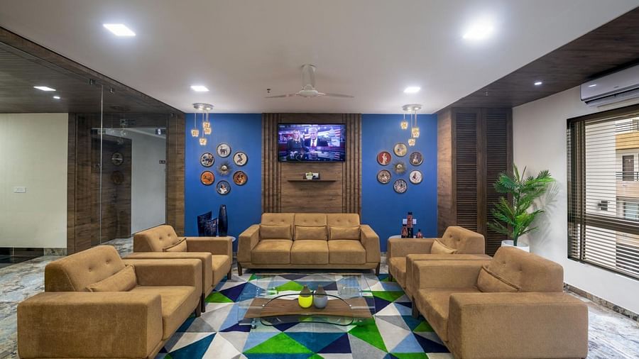 Lounge area with comfortable sofas, a patterned rug, and a television mounted on a decorative wall at Angel Lords Eco Inn Amreli.