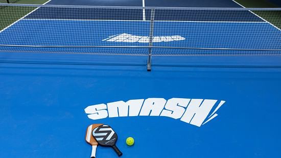 Close-up view of indoor pickleball courts with paddles and balls placed on a blue surface marked 'SMASH,' at Jenneys Residency, Coimbatore.
