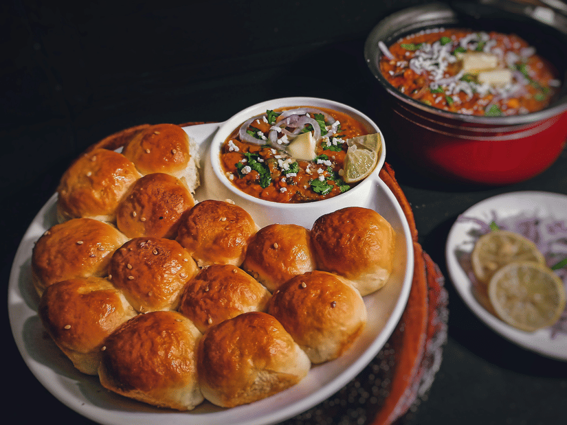 A traditional Indian pav bhaji meal featuring toasted, buttered bread buns served alongside a rich, spicy vegetable curry.