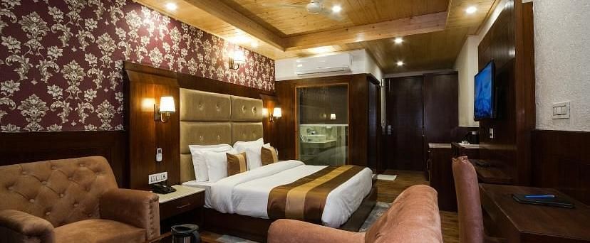 A expansive hotel room with a king size bed, two armchairs, and a small table in the centre | DLS La Serene Manali