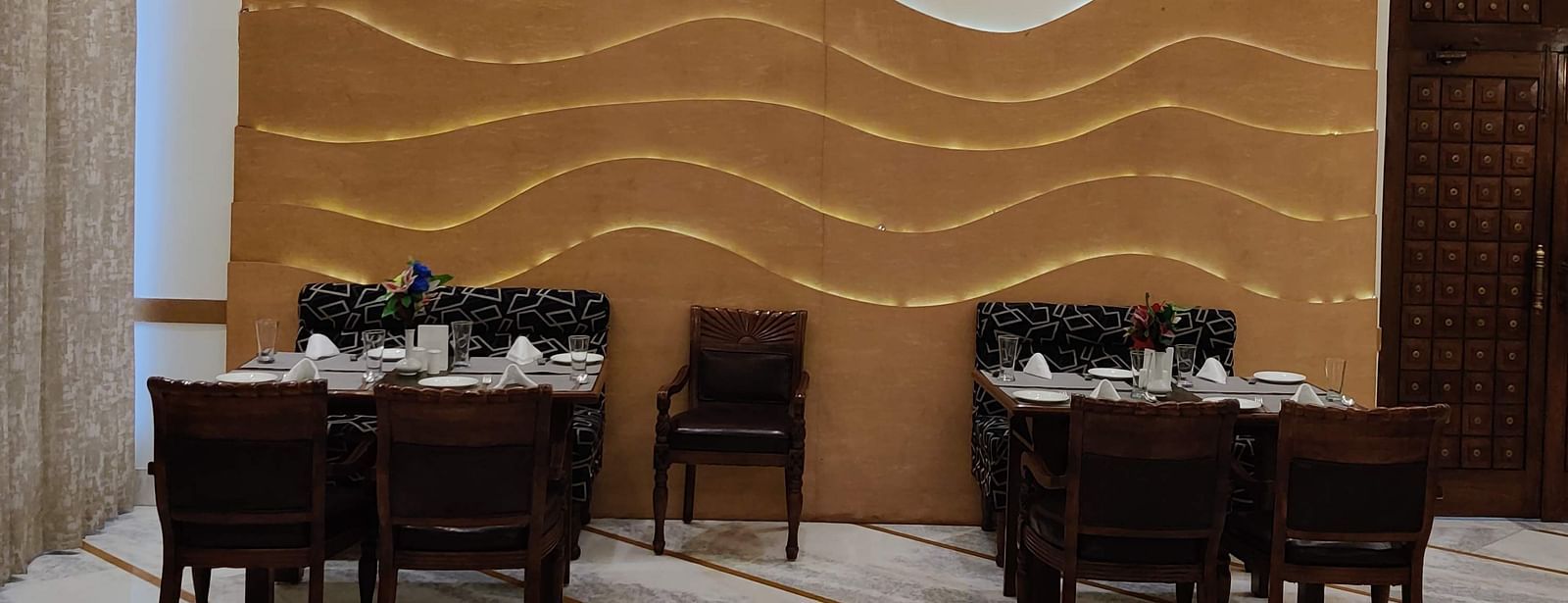 Two dining tables at the Gold Plate restaurant with a golden coloured mural on the wall - Hotel Gold, Panipat