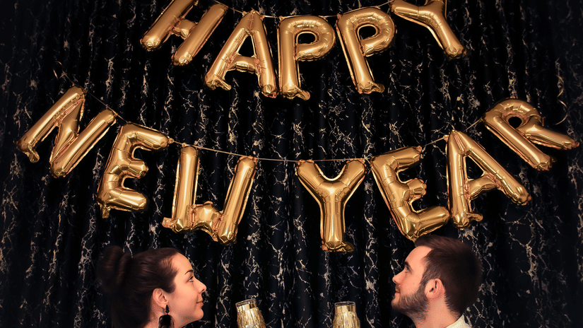 A couple holding drinks with happy new year made out of ballons on the wall