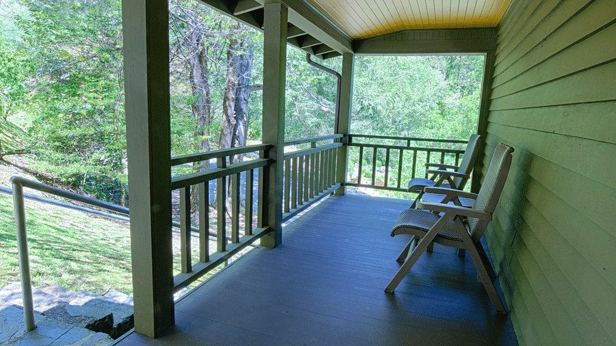 a wooden porch outside a cabin with two empty chairs overlooking the lush green surroundingsfull view image of a bedroom with wooden interiors featuring two beds - Historic Tapoco Lodge
