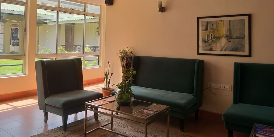 alt-text A cozy hotel lounge with green upholstered chairs, a coffee table, and a large window letting in natural light.