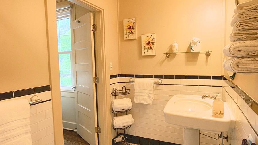 full view image of a compact bathroom with all necessary linens and toiletries and a door opening to the room - Historic Tapoco Lodge