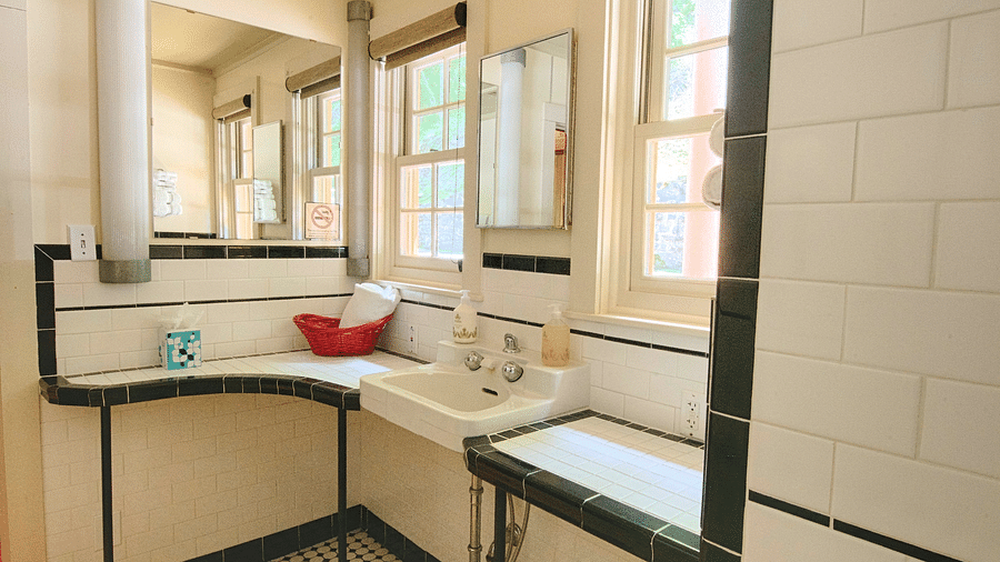 a bathroom with a small counter featuring a small wash basin with two medium sized windows besides it - Historic Tapoco Lodge
