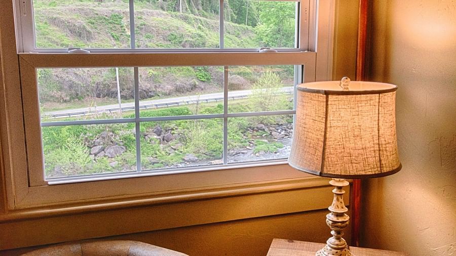a close up image of a leather arm chair kept alongside a wooden table with a lamp over it - Historic Tapoco Lodge