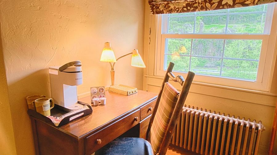 a writing desk and chair along with a table lamp kept besides a window - Historic Tapoco Lodge
