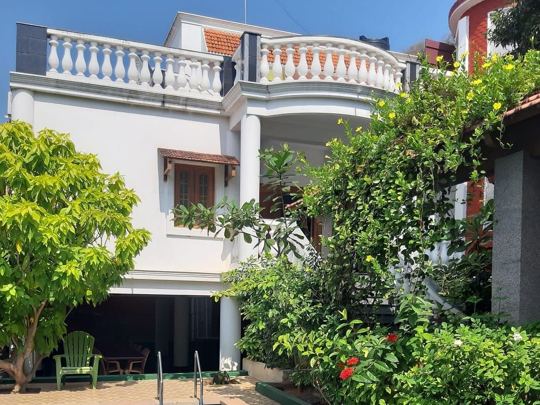 Facade of  Villa Serenity Le Sejour Pondicherry with a swimming pool in front and plants on the side.