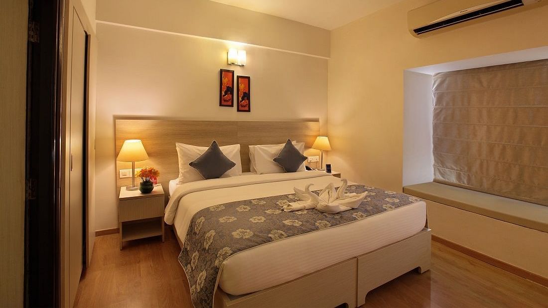 Premium room at Starlit Suites, Bangalore features a double bed with patterned bedding and cushions, bedside tables with lamps, and a window beside.