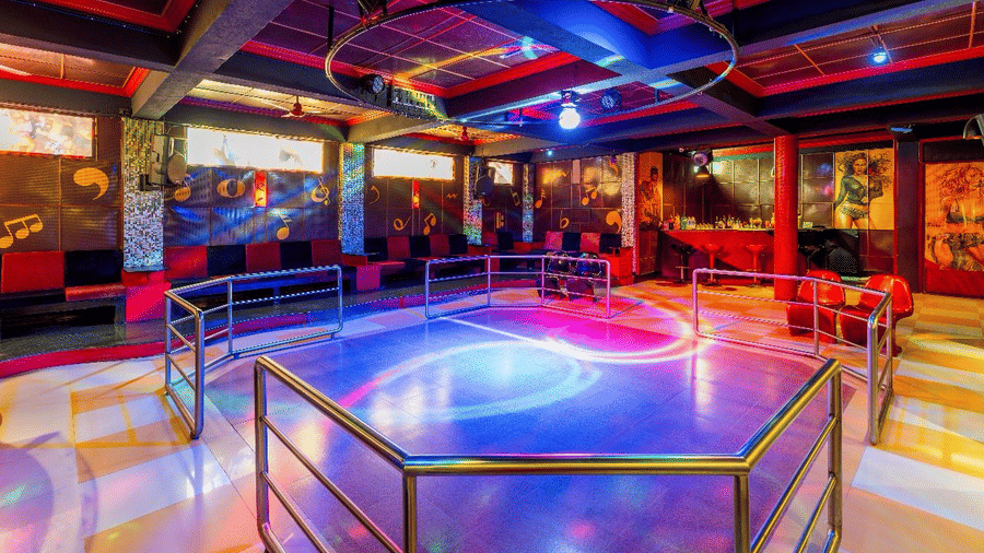 A dimly lit dance floor area featuring a metal railing enclosure, colourful illuminated flooring, and wall seating at Amantra Shilpi Resort, Udaipur.
