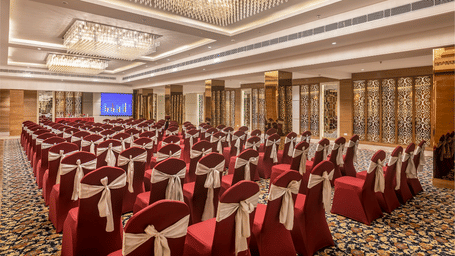 A spacious meeting hall with rows of red chairs facing a stage for a presentation - Lords Hotels & Resorts