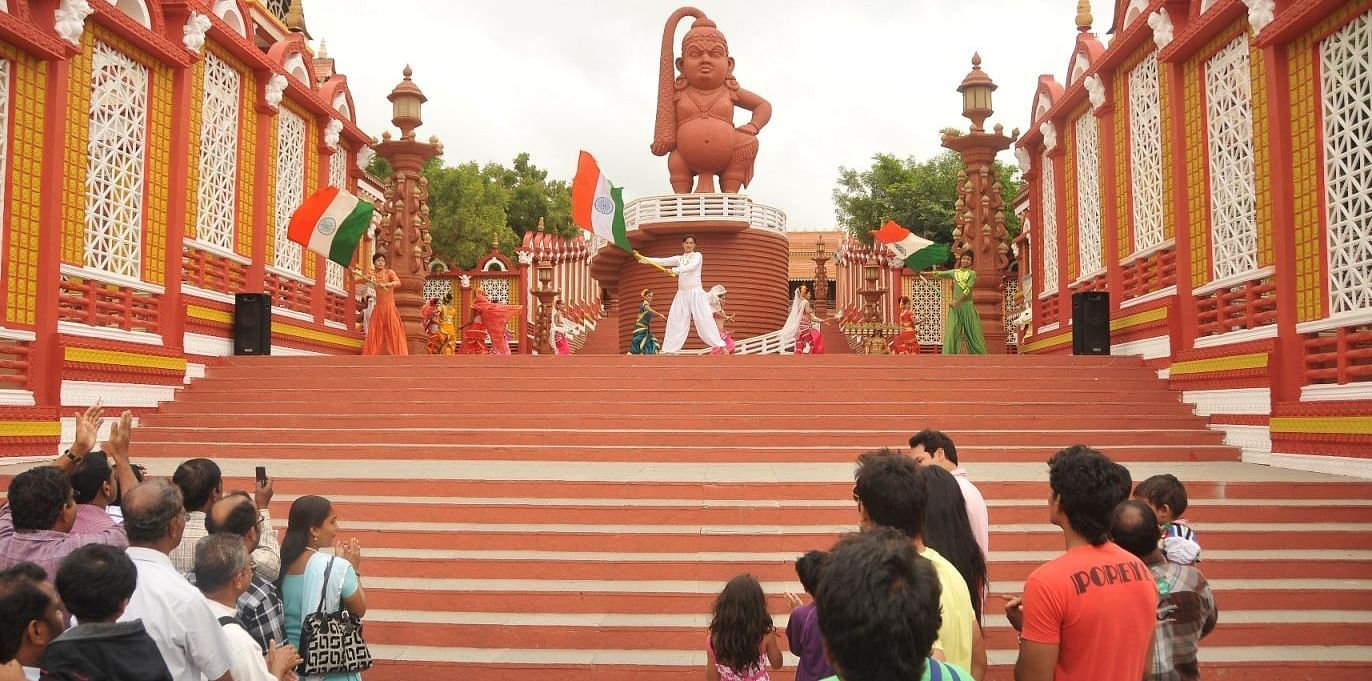 A crowd of people, including children, gathered at a vibrant cultural event in front of a large, ornate red and gold stage with a massive statue, celebrating a traditional festival at Ramoji Film City Hotels in Hyderabad 